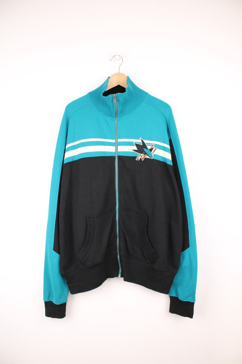 San Jose Sharks Zip Up Sweater in a black, blue and white colourway, full zip up with side pockets, stripes going across the front and the logo and spell out embroidered on the back.