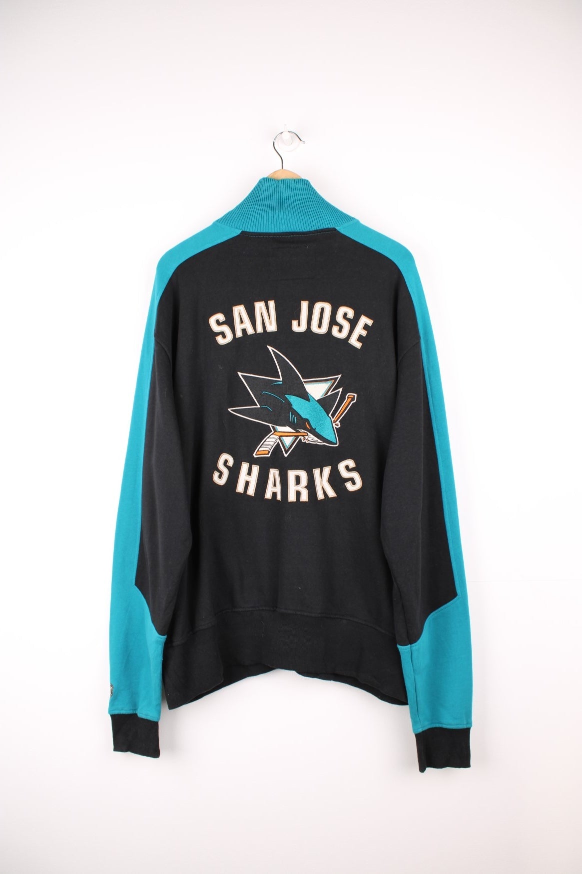 San Jose Sharks Zip Up Sweater in a black, blue and white colourway, full zip up with side pockets, stripes going across the front and the logo and spell out embroidered on the back.