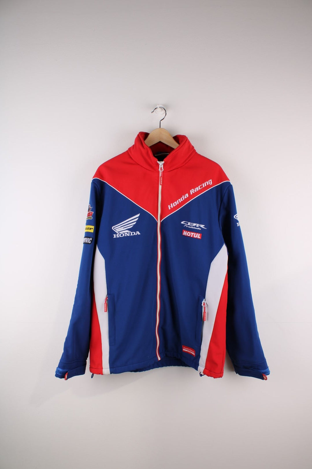 Vintage Honda Softshell Racing Jacket in a blue and red colourway, zips up and has side pockets, hidden hood, and the logos embroidered all over the jacket.