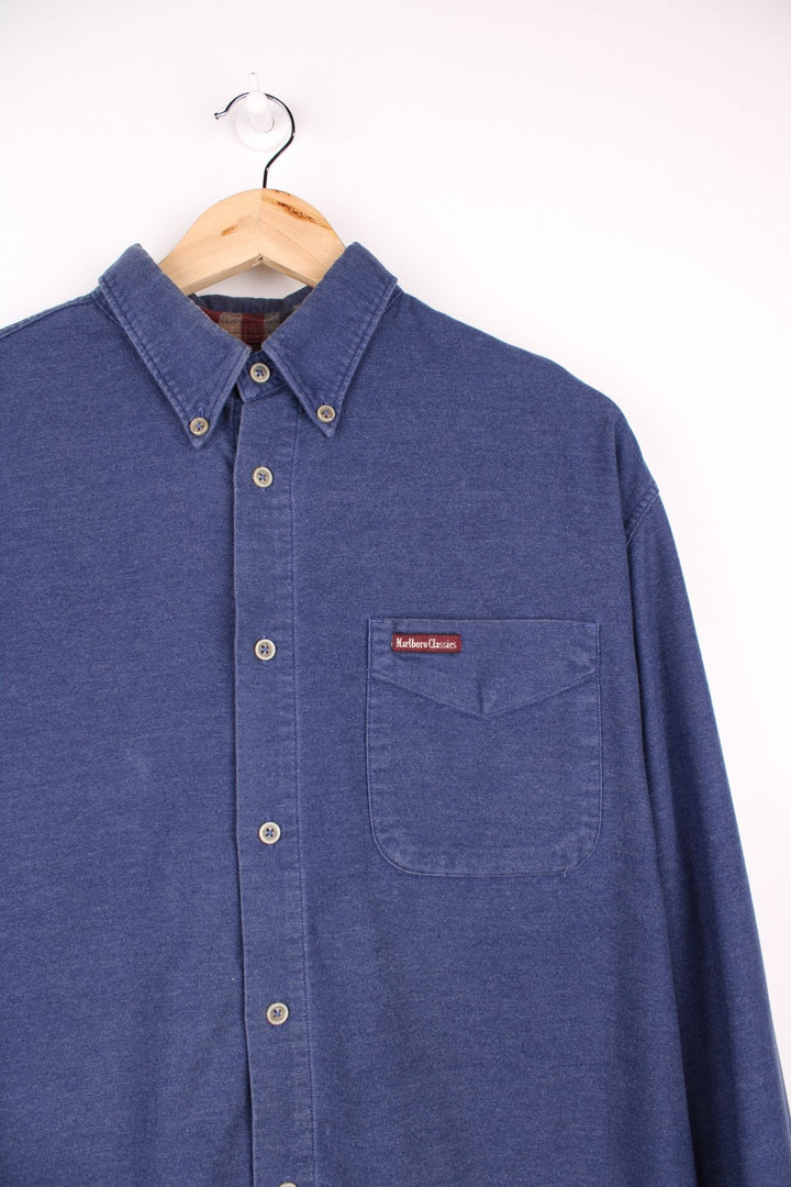 Marlboro Classics button-down shirt in blue with button closure, one chest pocket, and a small logo patch in red..