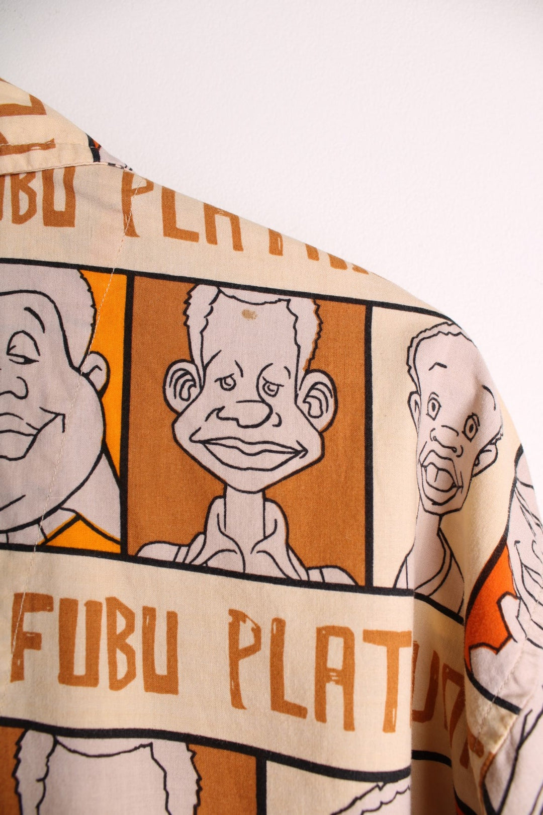 FUBU Platinum short-sleeved shirt in brown, orange and cream with cartoon print of Fat Albert and the Cosby Kids, button closure, one chest pocket, and a small logo tab in red.