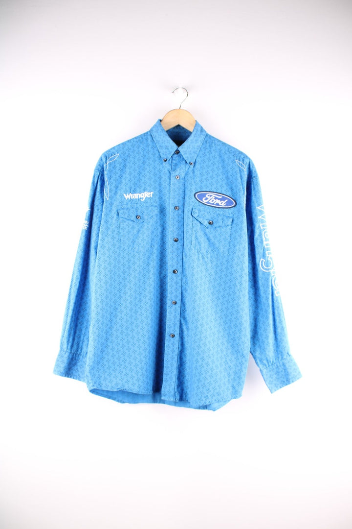 Wrangler button-down western shirt in blue with a western print, two buttoned pockets, white embroidery, and embroidered Ford and Wrangler logos on the front, sleeves, and yoke at the back.