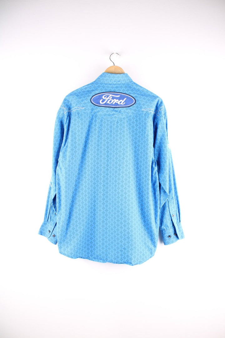 Wrangler button-down western shirt in blue with a western print, two buttoned pockets, white embroidery, and embroidered Ford and Wrangler logos on the front, sleeves, and yoke at the back.