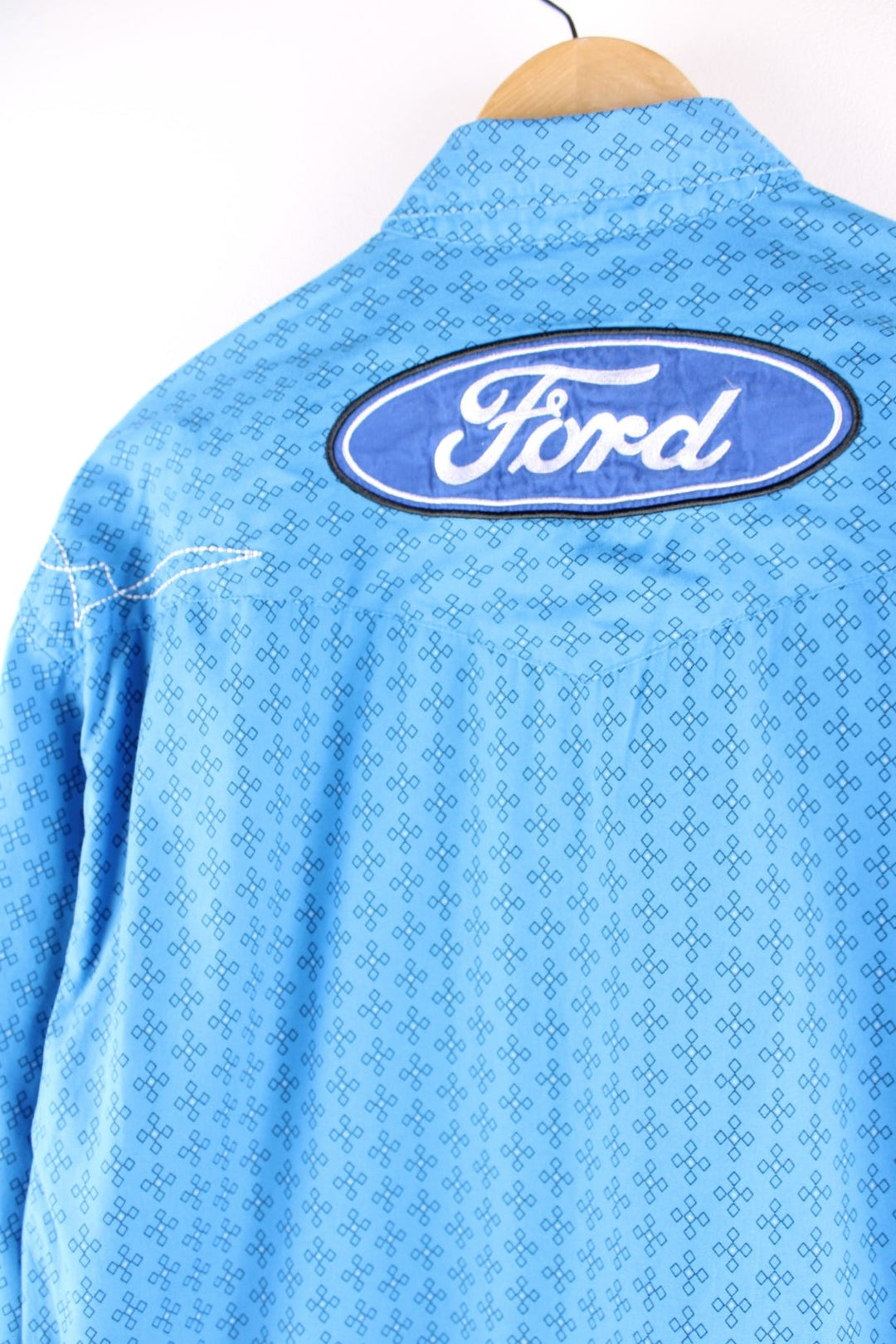 Wrangler button-down western shirt in blue with a western print, two buttoned pockets, white embroidery, and embroidered Ford and Wrangler logos on the front, sleeves, and yoke at the back.