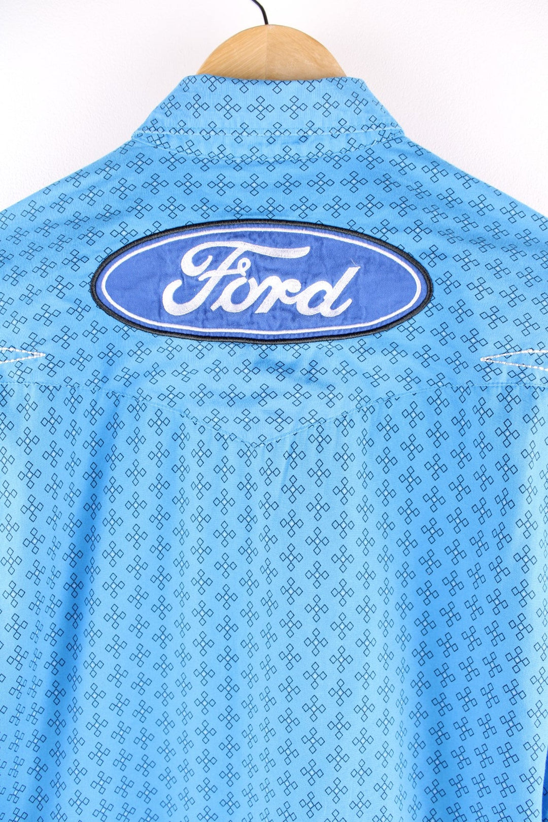 Wrangler button-down western shirt in blue with a western print, two buttoned pockets, white embroidery, and embroidered Ford and Wrangler logos on the front, sleeves, and yoke at the back.