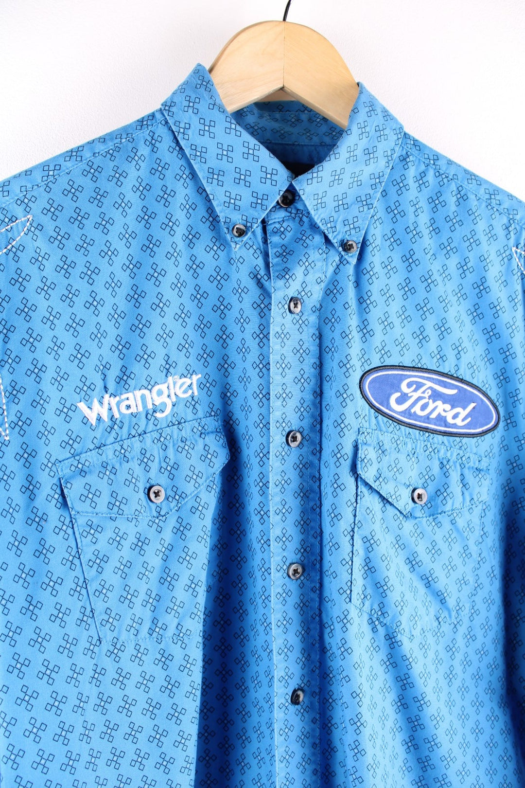 Wrangler button-down western shirt in blue with a western print, two buttoned pockets, white embroidery, and embroidered Ford and Wrangler logos on the front, sleeves, and yoke at the back.