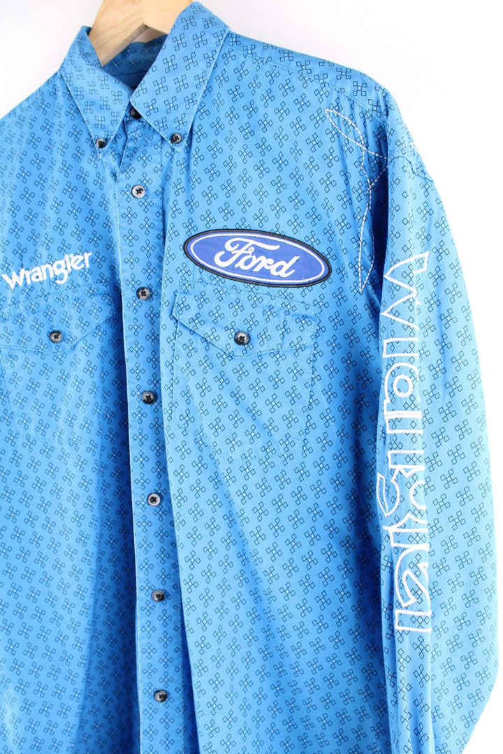 Wrangler button-down western shirt in blue with a western print, two buttoned pockets, white embroidery, and embroidered Ford and Wrangler logos on the front, sleeves, and yoke at the back.