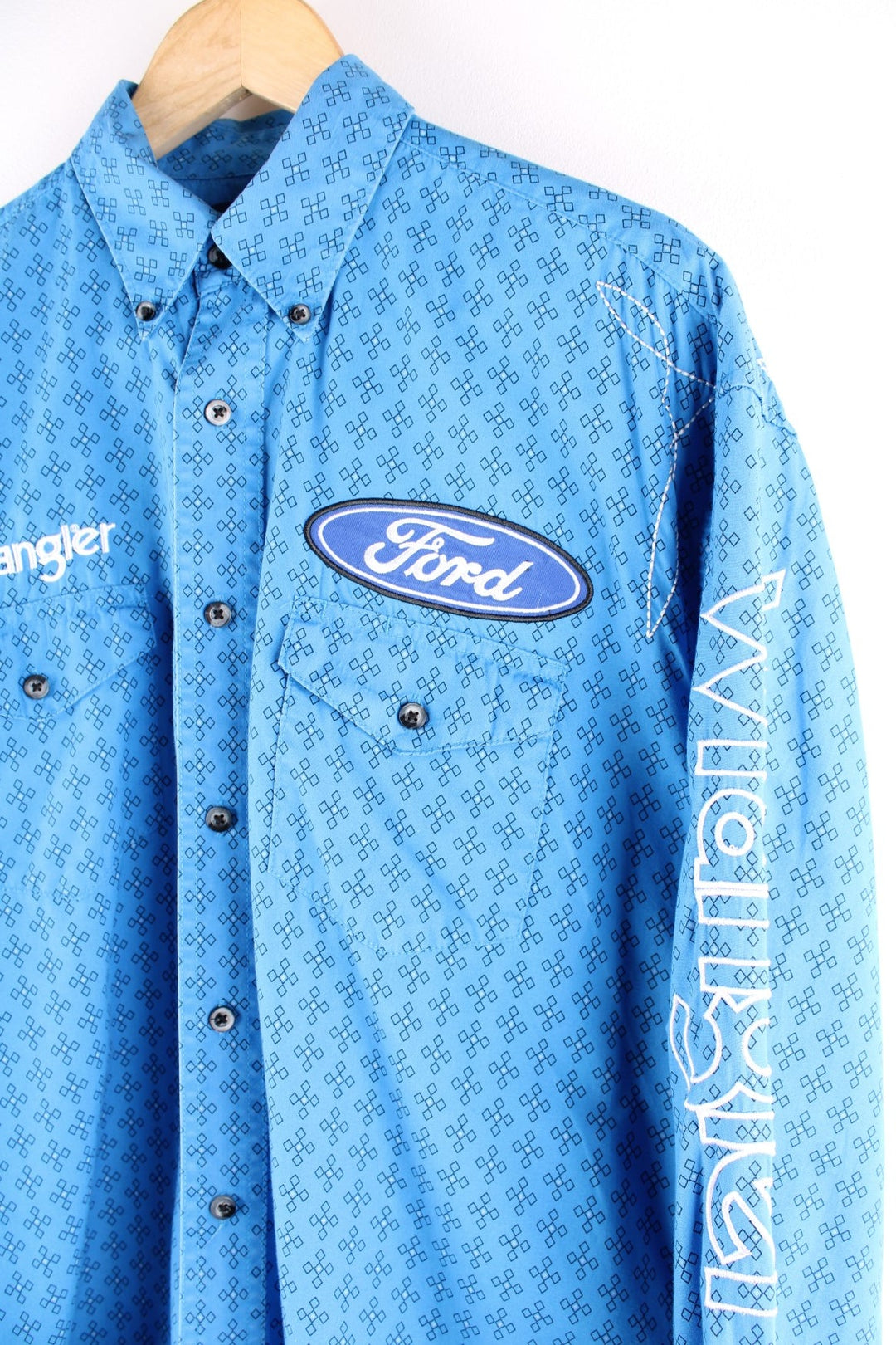 Wrangler button-down western shirt in blue with a western print, two buttoned pockets, white embroidery, and embroidered Ford and Wrangler logos on the front, sleeves, and yoke at the back.