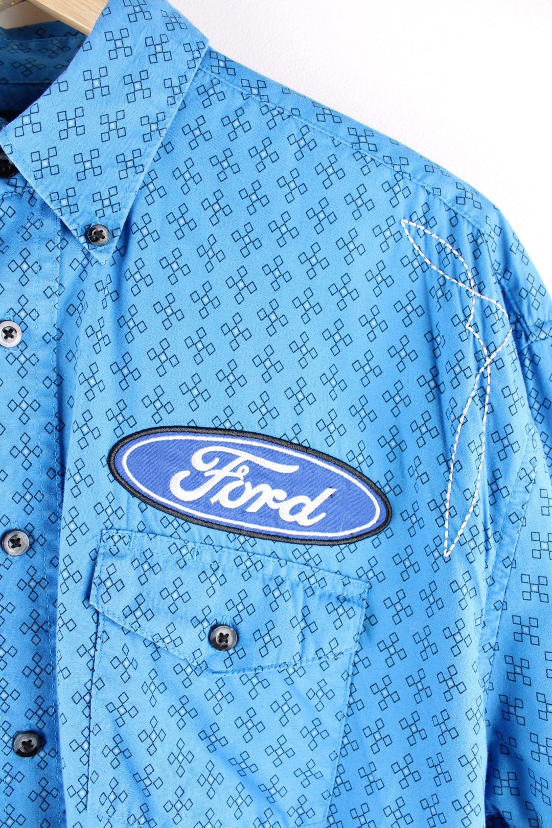 Wrangler button-down western shirt in blue with a western print, two buttoned pockets, white embroidery, and embroidered Ford and Wrangler logos on the front, sleeves, and yoke at the back.