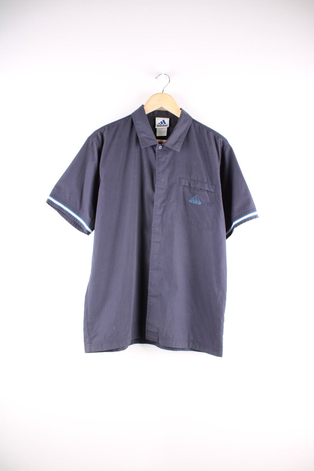 Adidas short-sleeved shirt in blue-grey with concealed button closure, white accent bands on the sleeves, one slit pocket on the chest, and an embroidered logo.