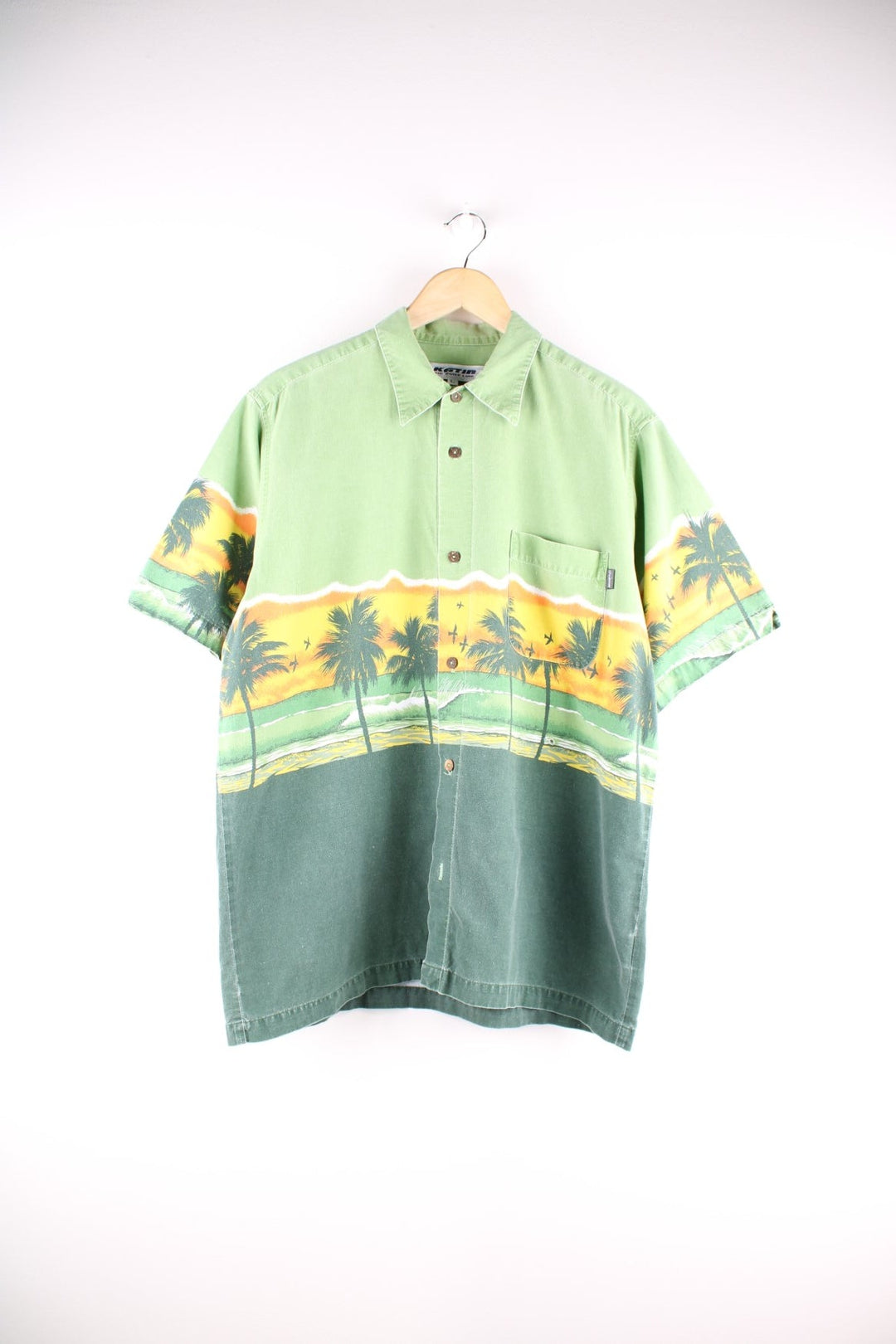 Vintage short-sleeved Hawaiian shirt in green with a front and back design of a beach at sunset, wood-effect buttons, one breast pocket, and a small tab of manufacturer Katin.