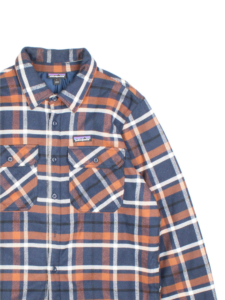 Patagonia Flannel Jacket in a blue, brown and white colourway, button up with double chest pockets, insulated with a quilted lining, and has the logo embroidered on the front.