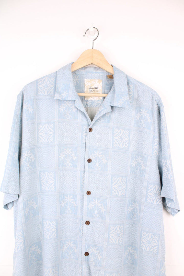 Pale blue hawaiian shirt by Tasso Elba, featuring tropical patterns and palm tree motifs in white, and brown wooden buttons.  