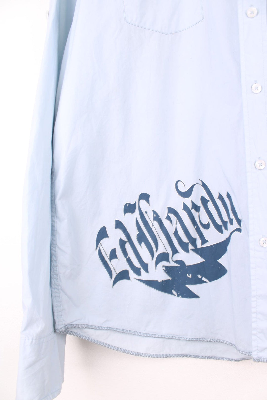 Pale blue long-sleeved button-down shirt by Ed Hardy, featuring double flap pockets, Ed Hardy spellout, tattoo-style eagle, tiger, roses and flames design on the back, skull motif on the collar and cuff lining, and an attached red brand tab on the left sleeve. 