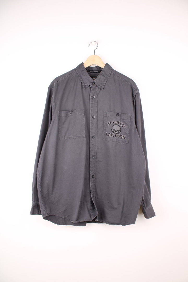 Dark grey Harley Davidson denim shirt with double patch pockets, buttons, and a skull motif and 'Harley Davidson' spellout embroidered on the front left pocket and on the back.  