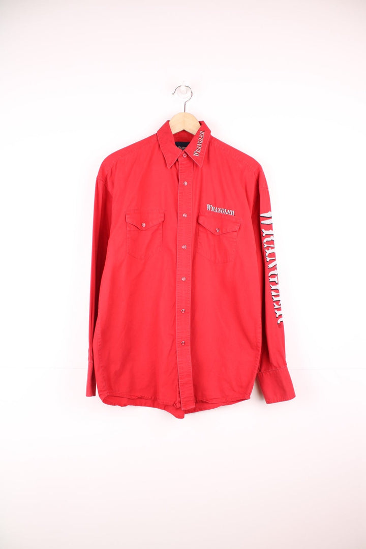 Vintage Wrangler red shirt with pearl snap fastenings and chest pockets. Features silver embroidered spell out logo on the collar, chest and sleeve. 