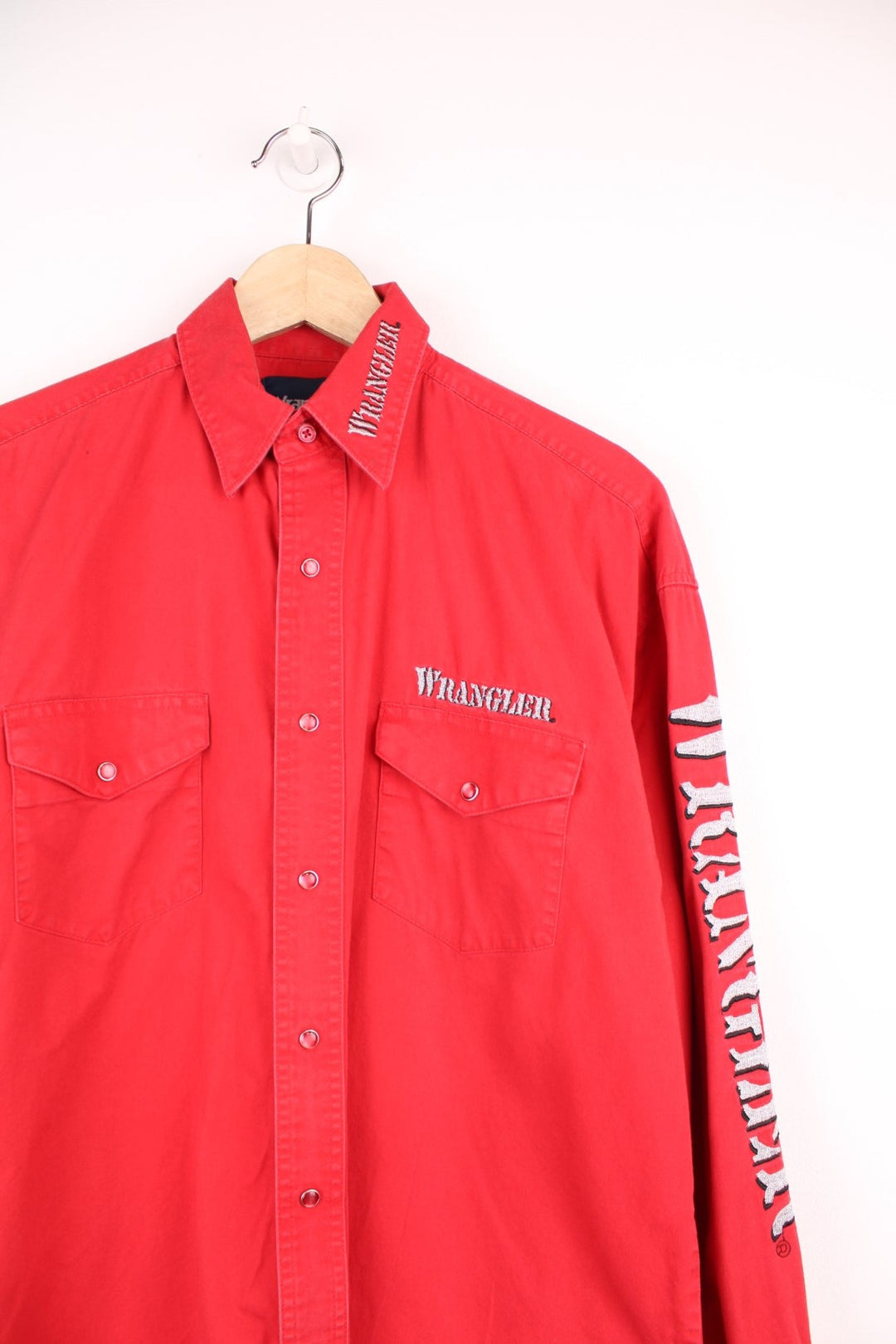 Vintage Wrangler red shirt with pearl snap fastenings and chest pockets. Features silver embroidered spell out logo on the collar, chest and sleeve. 