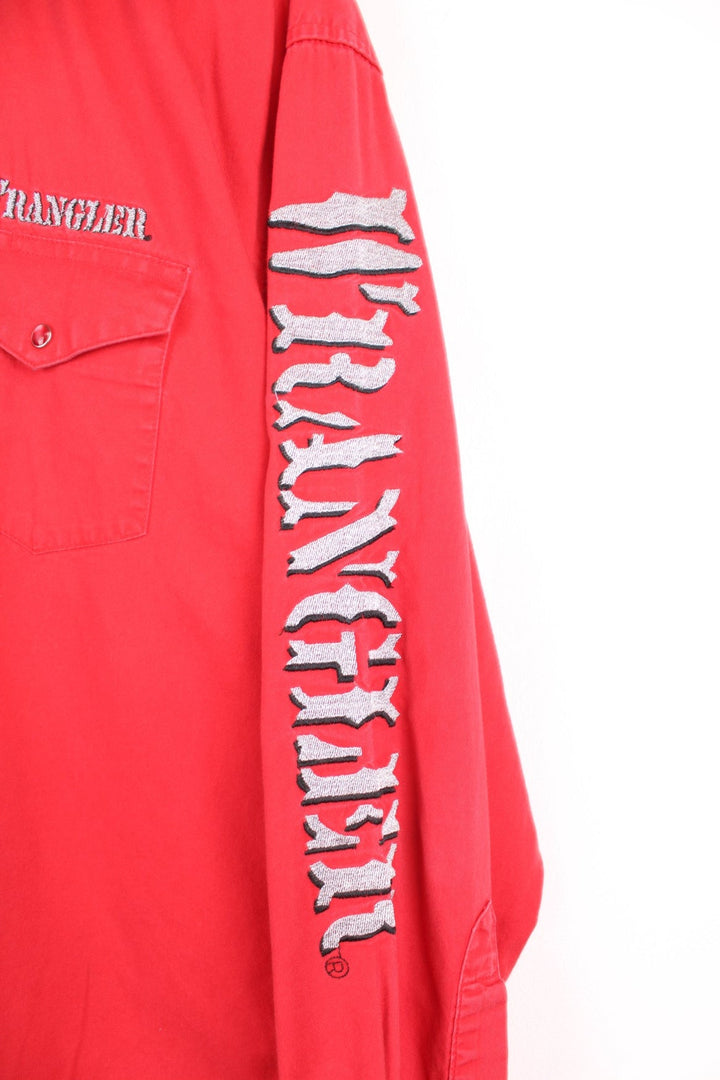 Vintage Wrangler red shirt with pearl snap fastenings and chest pockets. Features silver embroidered spell out logo on the collar, chest and sleeve. 