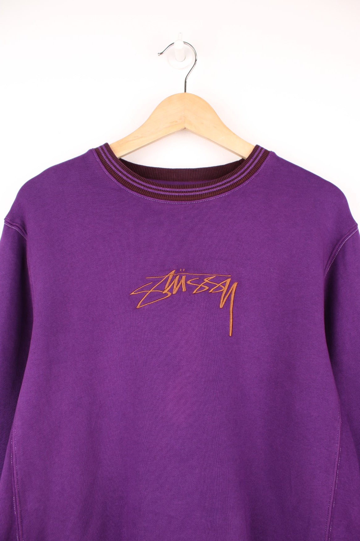 Stussy crew neck sweatshirt in purple with a contrast collar and embroidered logo across the chest in brown.