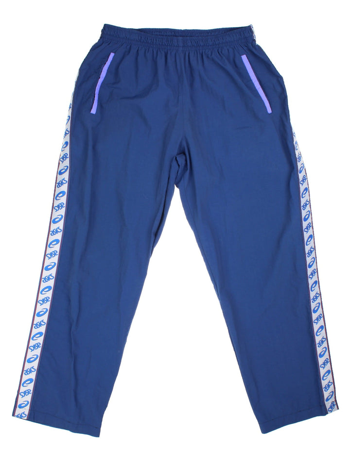 Asics tracksuit bottoms in navy blue with purple accents, logo tape down the legs, an elasticated waistband, and two pockets.