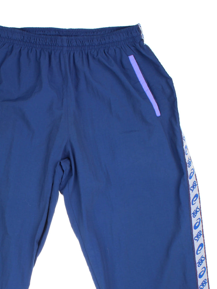 Asics tracksuit bottoms in navy blue with purple accents, logo tape down the legs, an elasticated waistband, and two pockets.