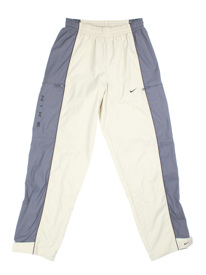 Nike 90s tracksuit bottoms in tan and grey with two zipped pockets, an elasticated waist, and an embroidered swoosh logo.