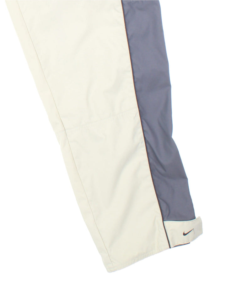 Nike 90s tracksuit bottoms in tan and grey with two zipped pockets, an elasticated waist, and an embroidered swoosh logo.