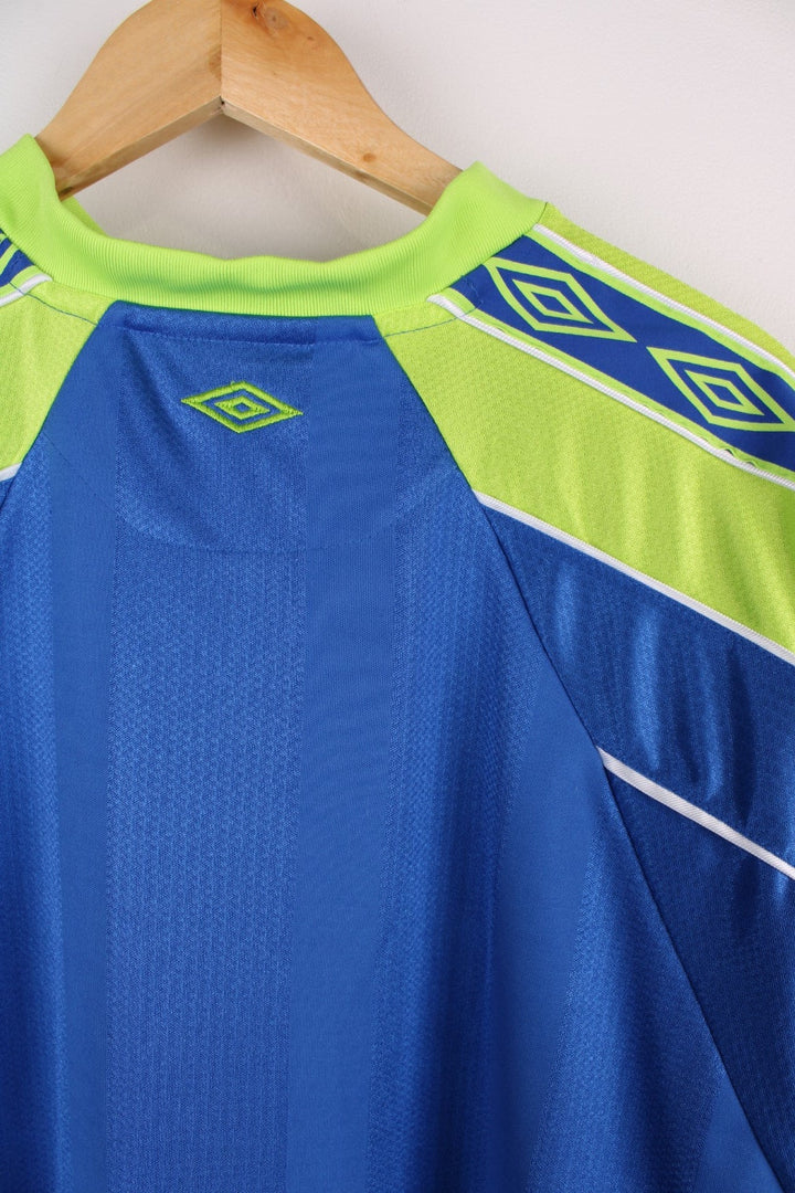 Vintage 1990s Umbro T-Shirt in ablue colourway with lime green accents and white piping on the shoulders and sleeves. The shirt has the Umbro logo embroidered on the front. 