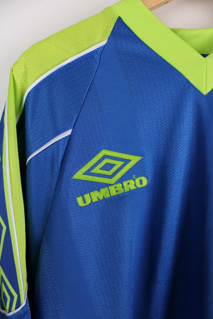 Vintage 1990s Umbro T-Shirt in ablue colourway with lime green accents and white piping on the shoulders and sleeves. The shirt has the Umbro logo embroidered on the front. 