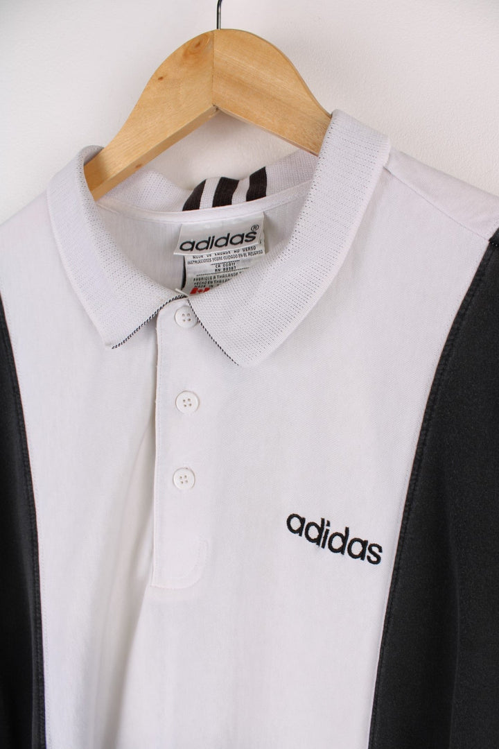 Vintage Adidas polo shirt in a white colourway with black panels on the sides and sleeves. The shirt has three stripes down the back, and the Adidas logo embroidered on the front. .