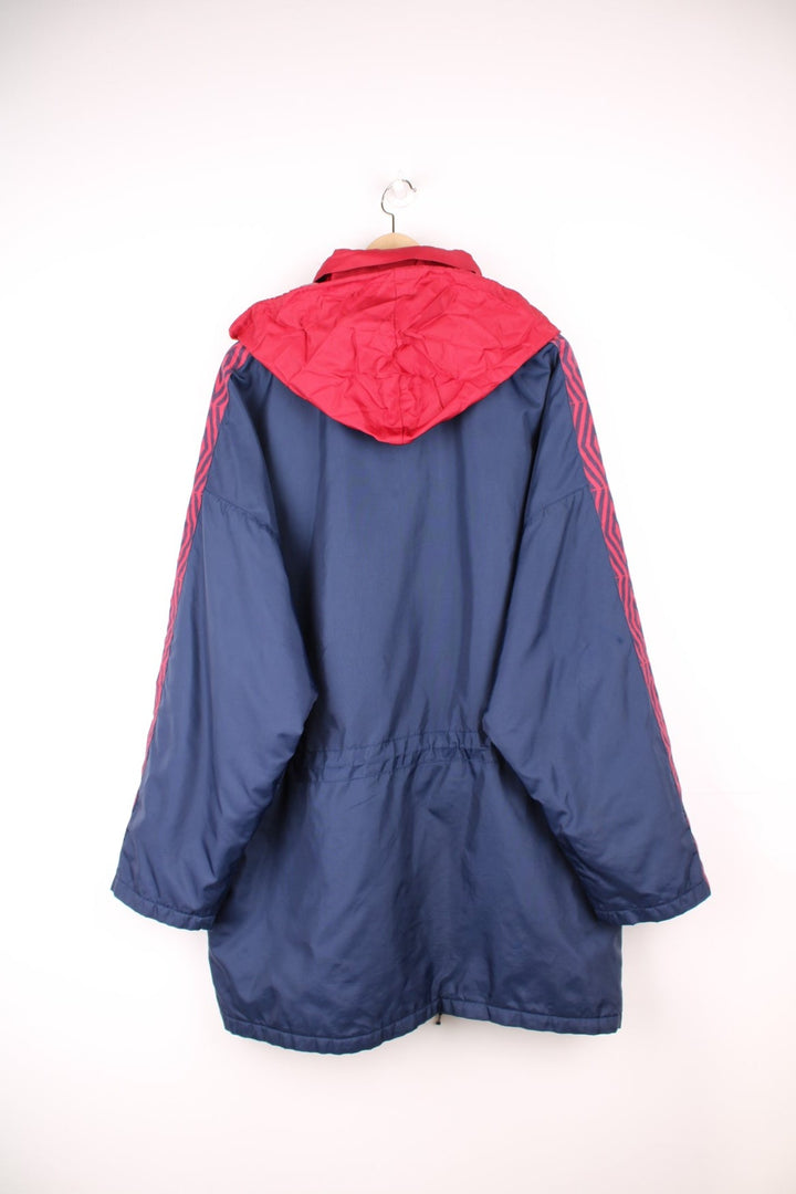 Umbro Training Coat in a navy blue and red colourway, zip up with multiple pockets, hidden hood, insulated, and has the logo embroidered on the front. 