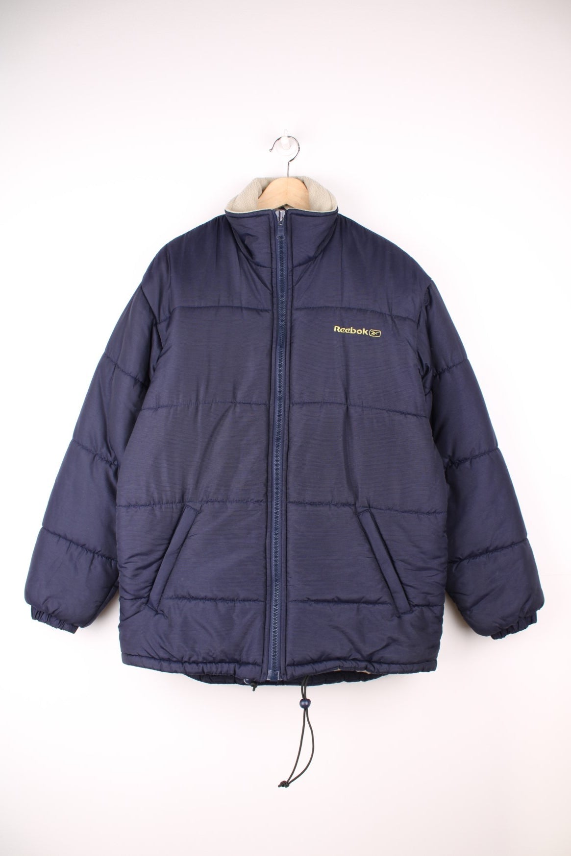 Reebok Puffer Coat in a blue colourway, zip up with side pockets, insulated lining, and has the logo embroidered on the front and back. 