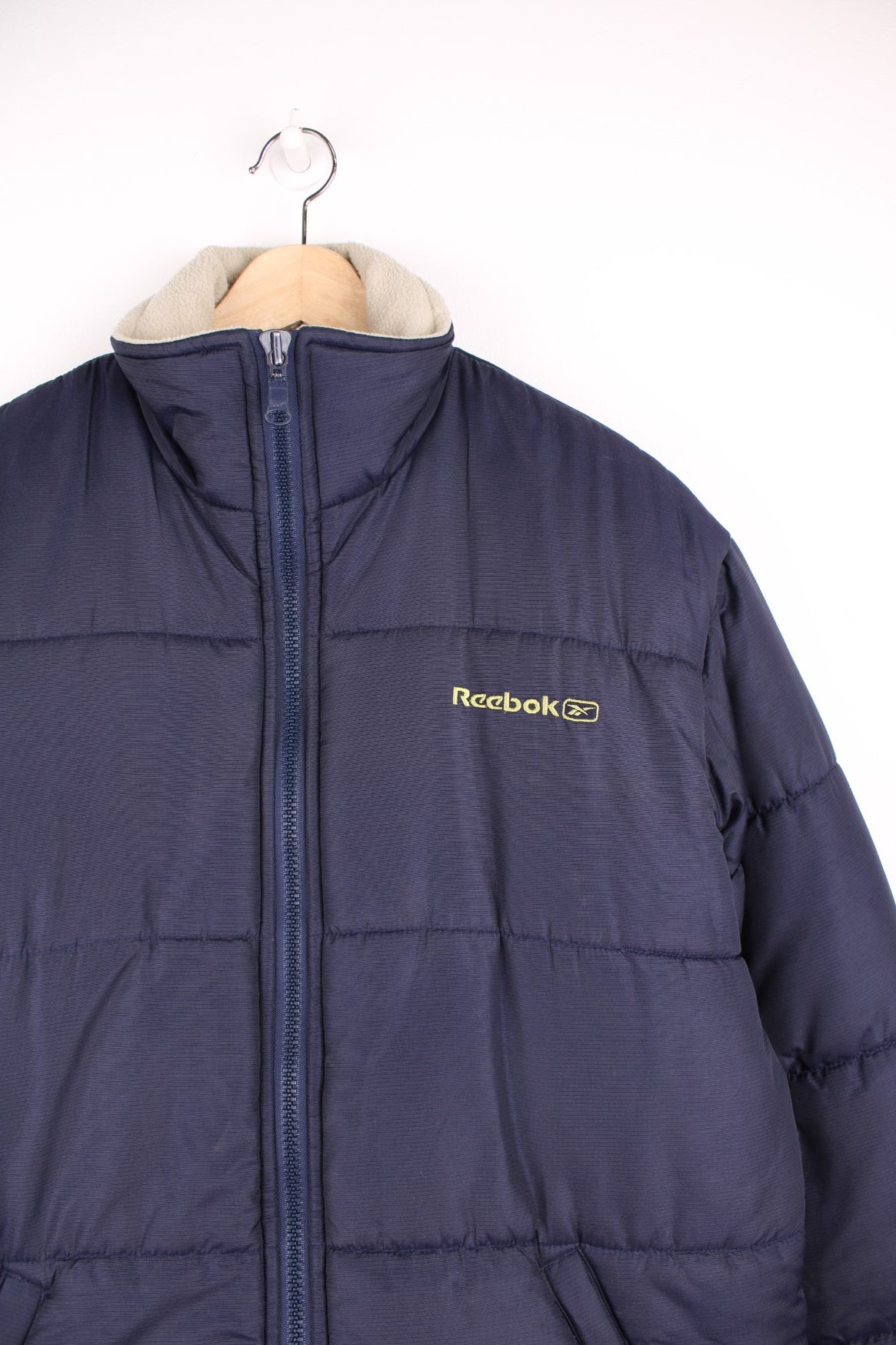 Reebok Puffer Coat in a blue colourway, zip up with side pockets, insulated lining, and has the logo embroidered on the front and back. 