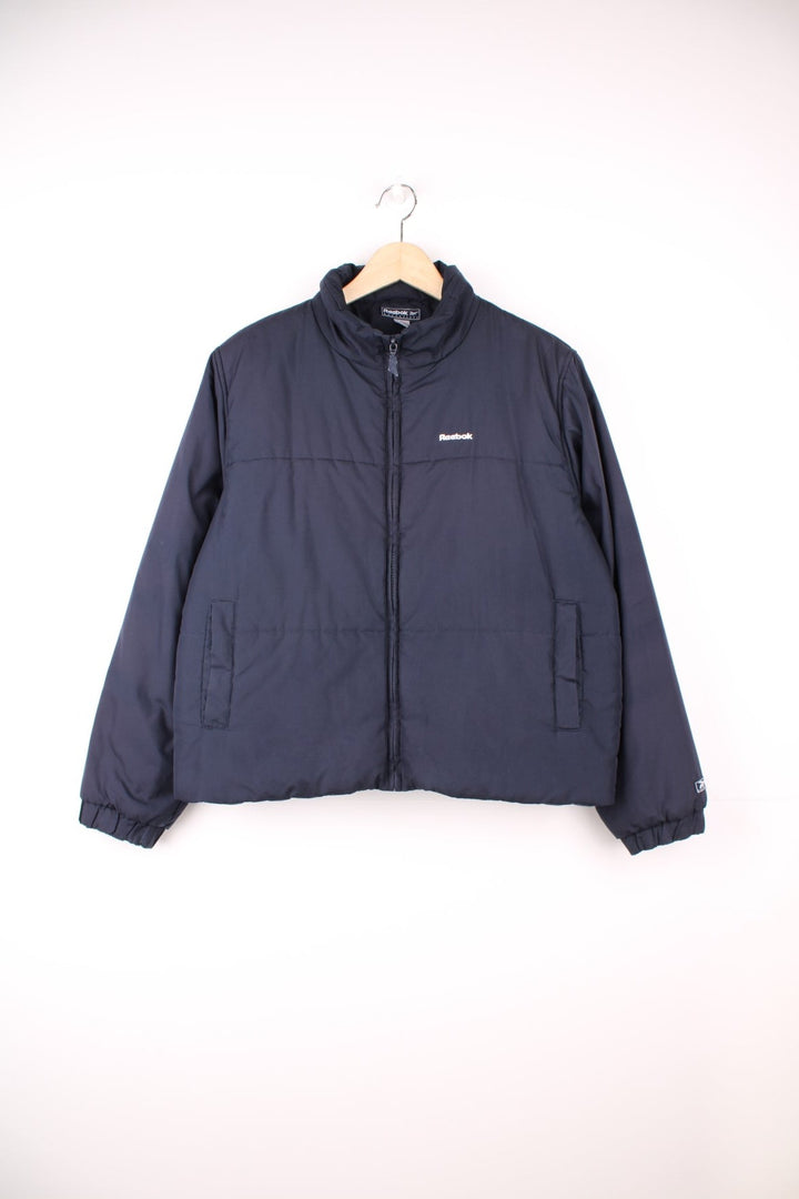 Reebok Puffer Coat in a navy blue colourway, zip up with side pockets, insulated lining, and has the logo embroidered on the front. 