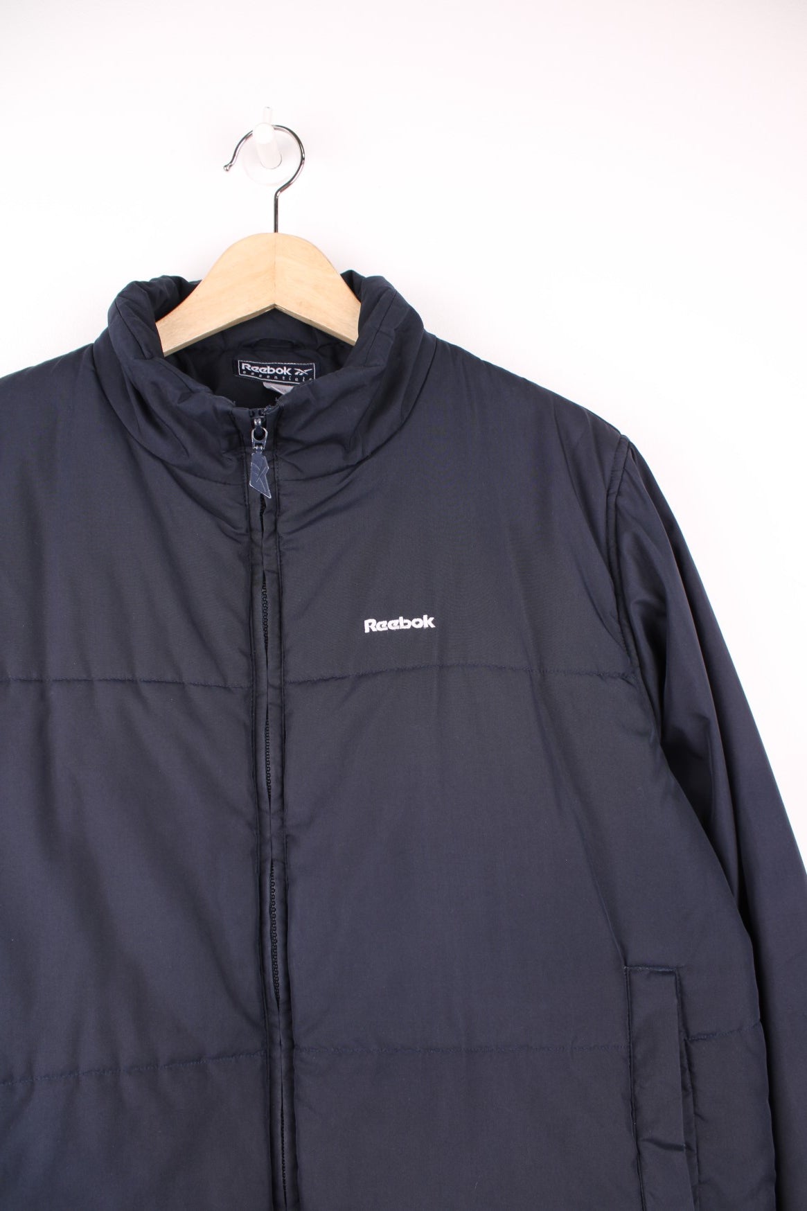 Reebok Puffer Coat in a navy blue colourway, zip up with side pockets, insulated lining, and has the logo embroidered on the front. 