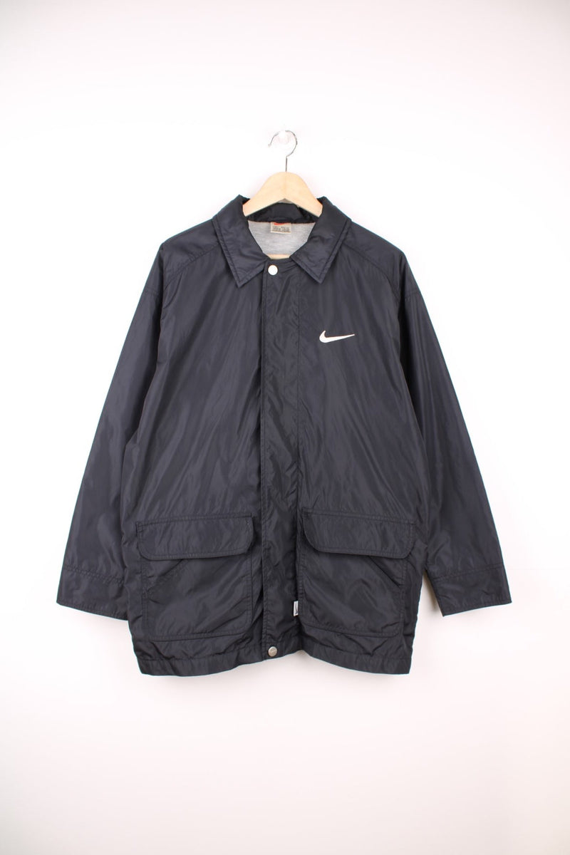 Nike Coach Jacket in a black and white colourway, zip up with side pockets, cotton lining, and has the swoosh logo embroidered on the front and back.