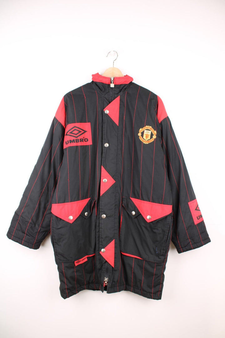 1993/95 Manchester United Umbro Training Coat in a black and red colourway with stripes throughout, zip up with side pockets, insulated with a quilted lining, and has the logos embroidered on the front and back.