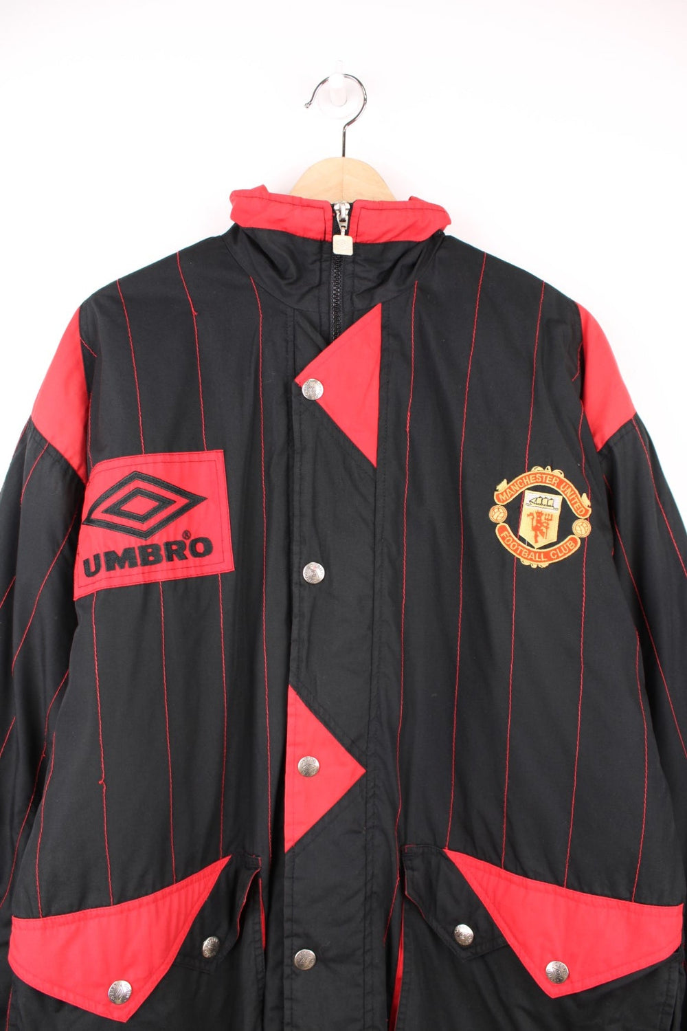 1993/95 Manchester United Umbro Training Coat in a black and red colourway with stripes throughout, zip up with side pockets, insulated with a quilted lining, and has the logos embroidered on the front and back.