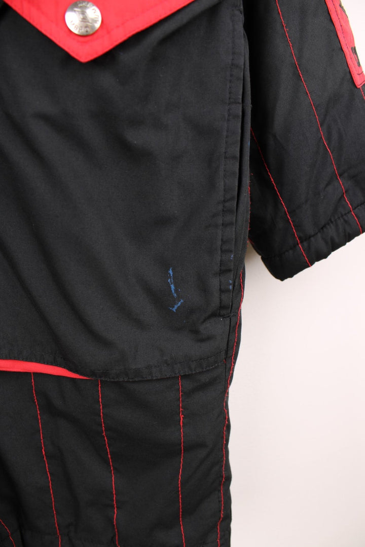 1993/95 Manchester United Umbro Training Coat in a black and red colourway with stripes throughout, zip up with side pockets, insulated with a quilted lining, and has the logos embroidered on the front and back.