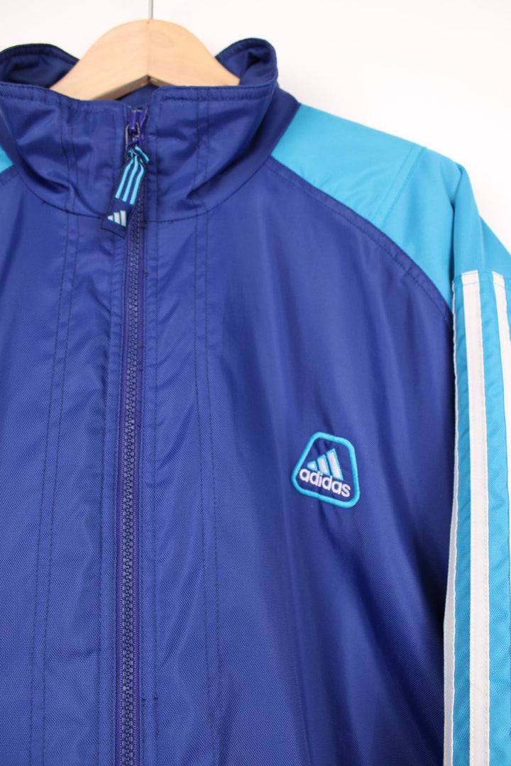 Adidas Training Jacket in a blue colourway with the iconic three stripes going down the sleeves, zip up with side pockets, and has the logo embroidered on the front. 