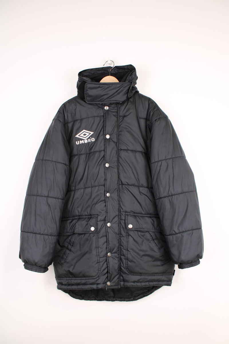 Vintage Umbro Puffer Coat in a black colourway, zip up with side pockets, has a detachable hood, insulated, and has the logo embroidered on the front. 