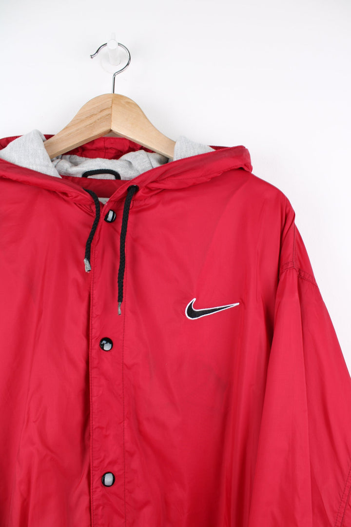 Red Nike coat with popper fastenings. Features embroidered logo on the chest and back. 