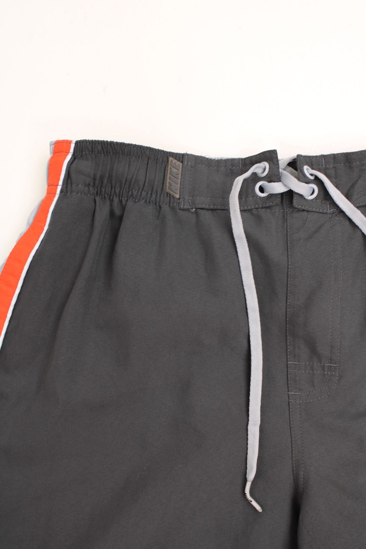 Nike Shorts in a grey, orange and white colourway with stripes going around the back and sides, has an ajdustable waist, side pockets, netted lining, and the logo embroidered on the back. 