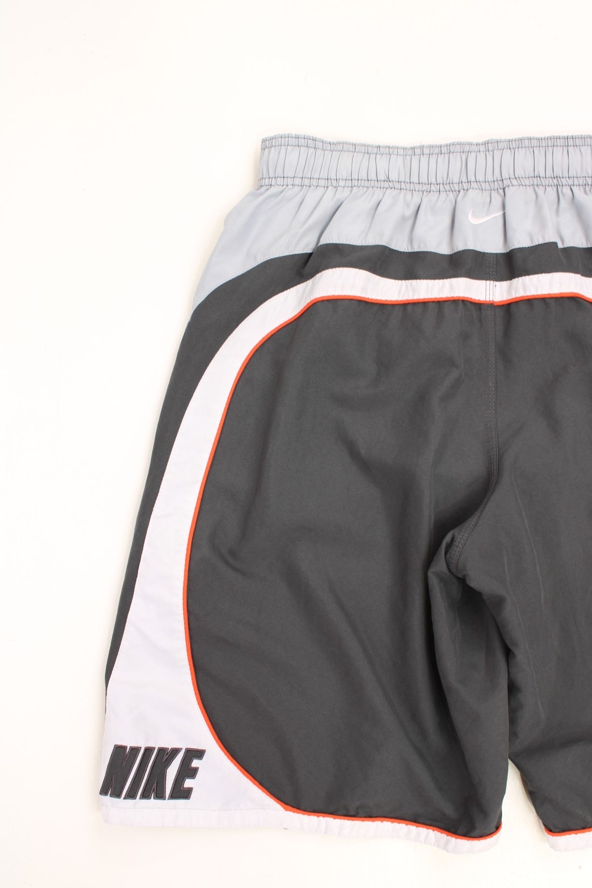 Nike Shorts in a grey, orange and white colourway with stripes going around the back and sides, has an ajdustable waist, side pockets, netted lining, and the logo embroidered on the back. 