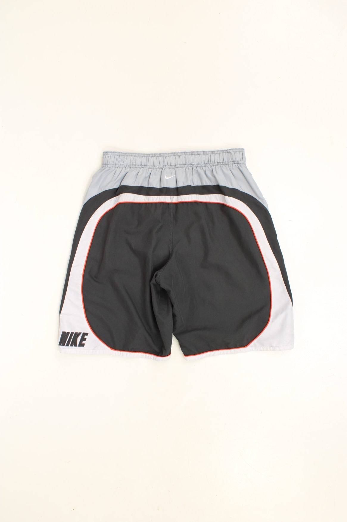 Nike Shorts in a grey, orange and white colourway with stripes going around the back and sides, has an ajdustable waist, side pockets, netted lining, and the logo embroidered on the back. 