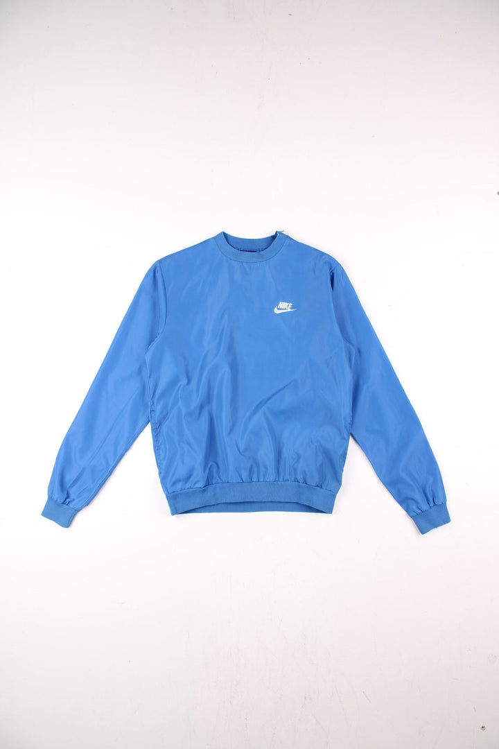 Vintage Nike pullover drill / training top in a blue shower-proof material, with two pockets, an embroidered swoosh logo, and a zipped opening on the left shoulder.