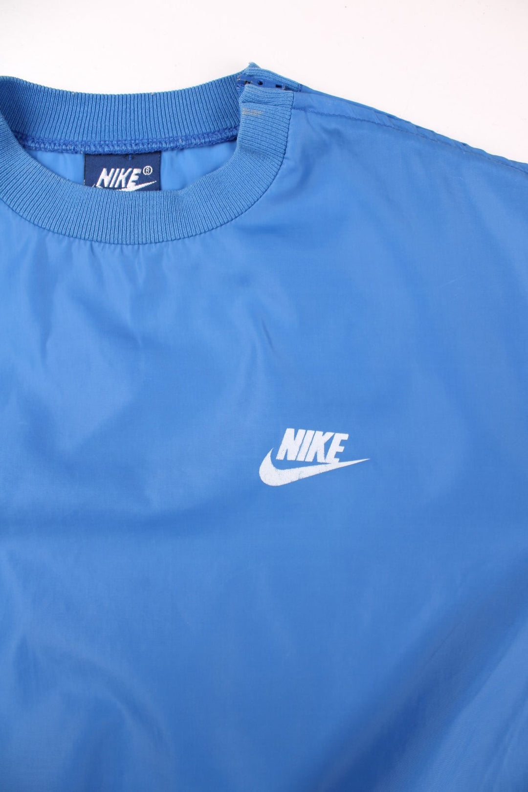 Vintage Nike pullover drill / training top in a blue shower-proof material, with two pockets, an embroidered swoosh logo, and a zipped opening on the left shoulder.