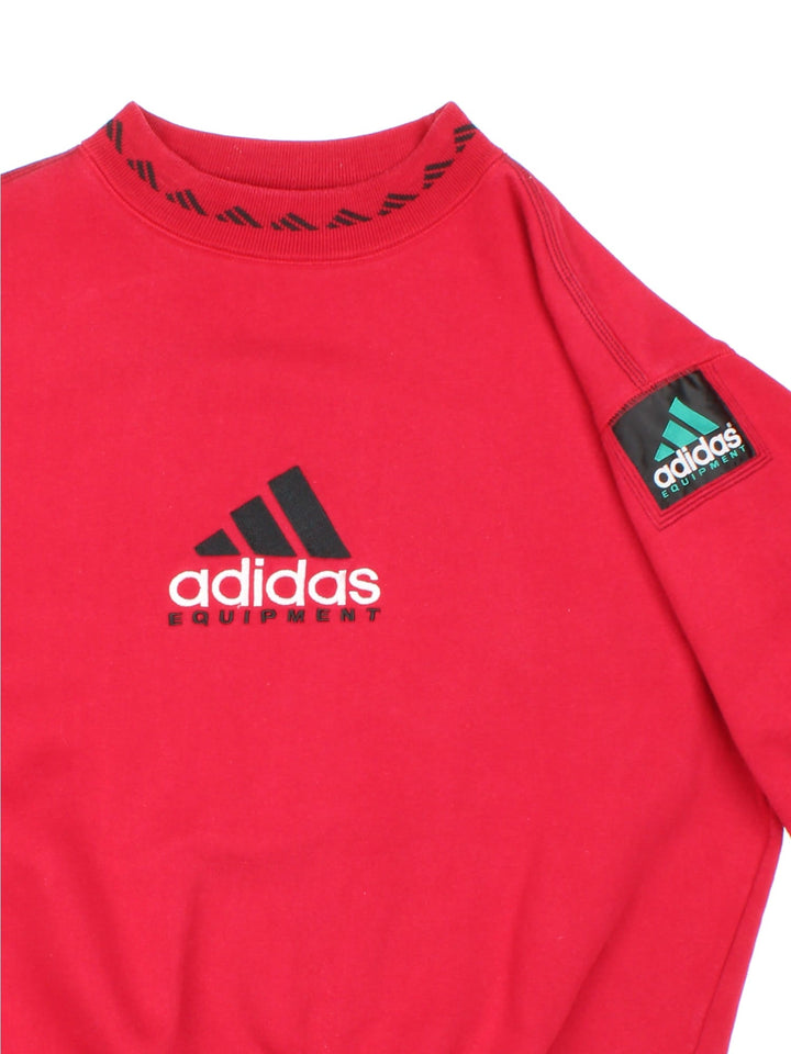 Vintage 1990s Adidas Sweatshirt in a red colourway with the logo embroidered on the front and centre. There is also an Adidas equipment patch sewn onto the sleeve. The sweatshirt has an elasticated graphic printed collar. 