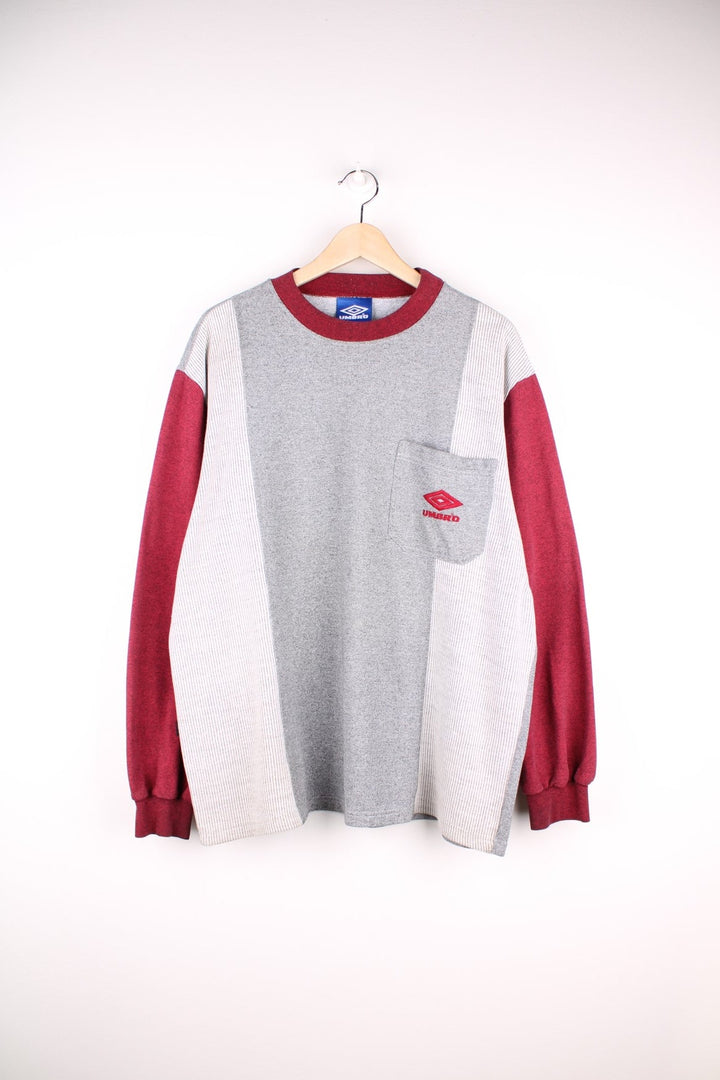 Umbro sweatshirt in grey with sleeves, collar, and embroidered logo in red, a black logo patch on the back, and one breast pocket. 