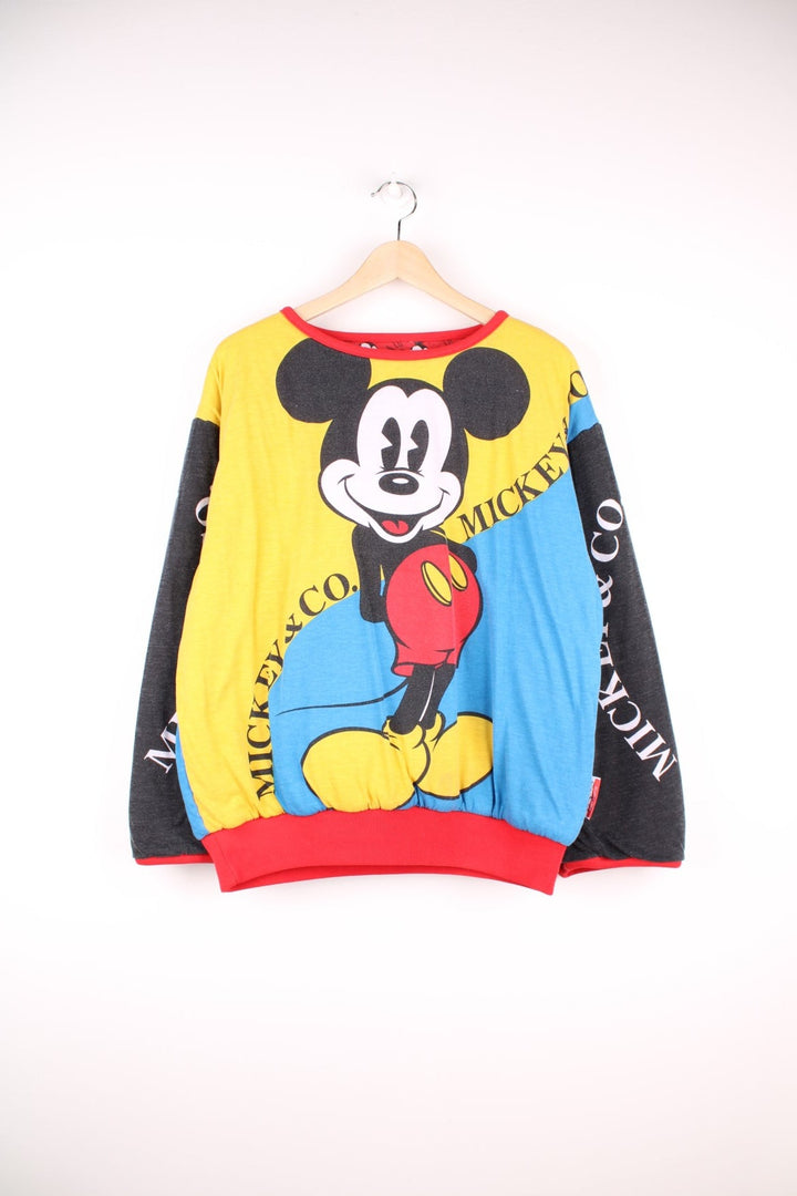 80s/90s Disney reversible lined sweatshirt with one red, yellow, and blue colourblocking side featuring a large Mickey Mouse graphic and text reading 'Mickey and Co.', and one red side with a repeating Mickey head pattern. 